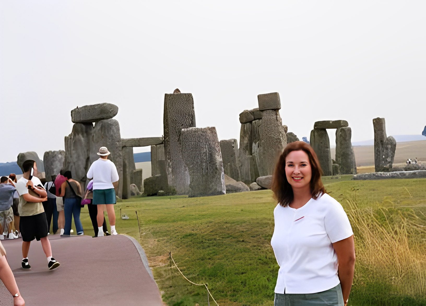 Woman smiling near Stonehenge with tourists nearby.