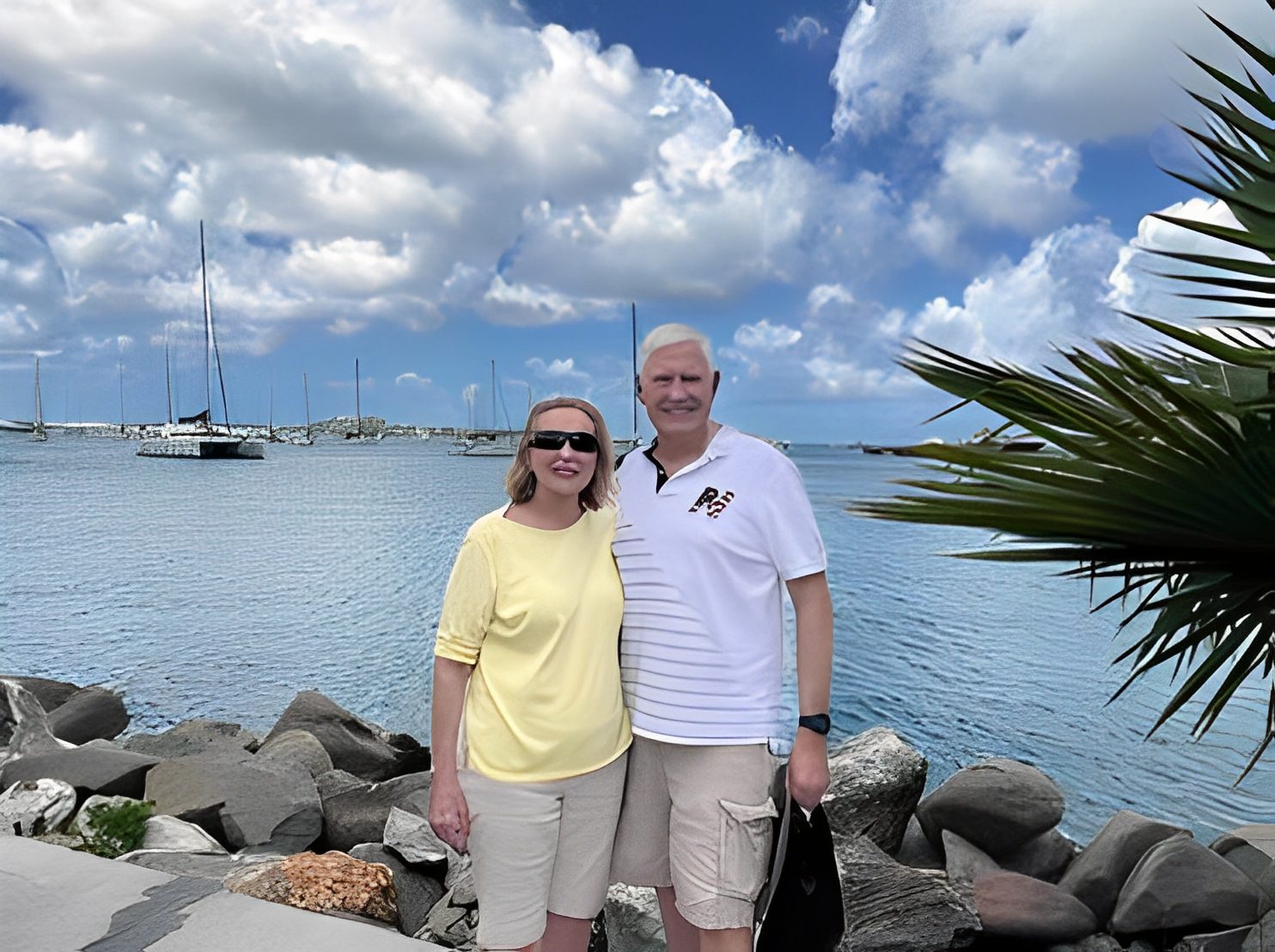 Couple posing by waterfront with sailboats.