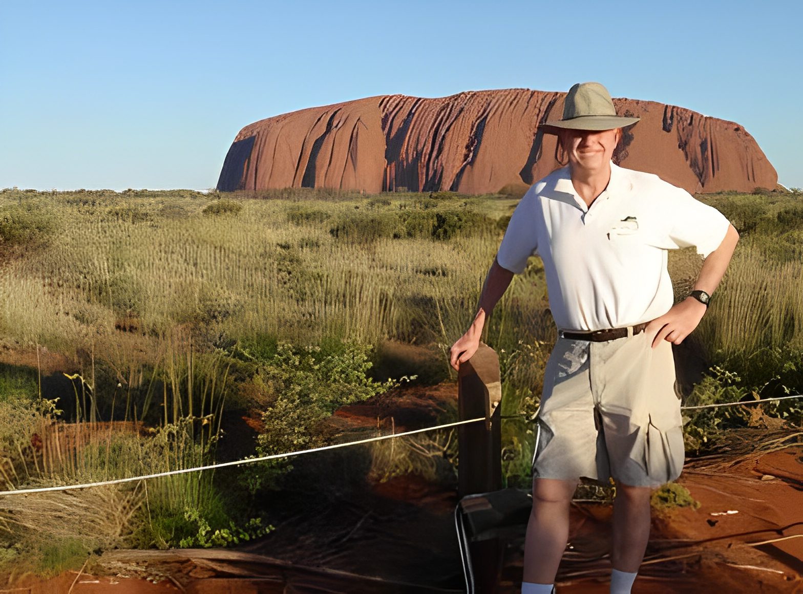 Man posing in front of Uluru rock formation.