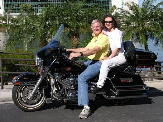 Couple riding motorcycle near palm trees.