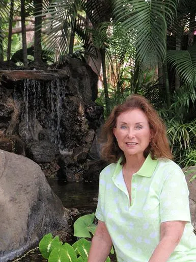 Woman smiling near a waterfall and plants.