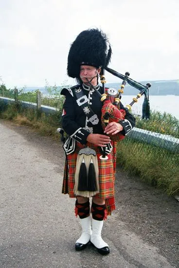 Bagpiper in traditional Scottish attire on road.