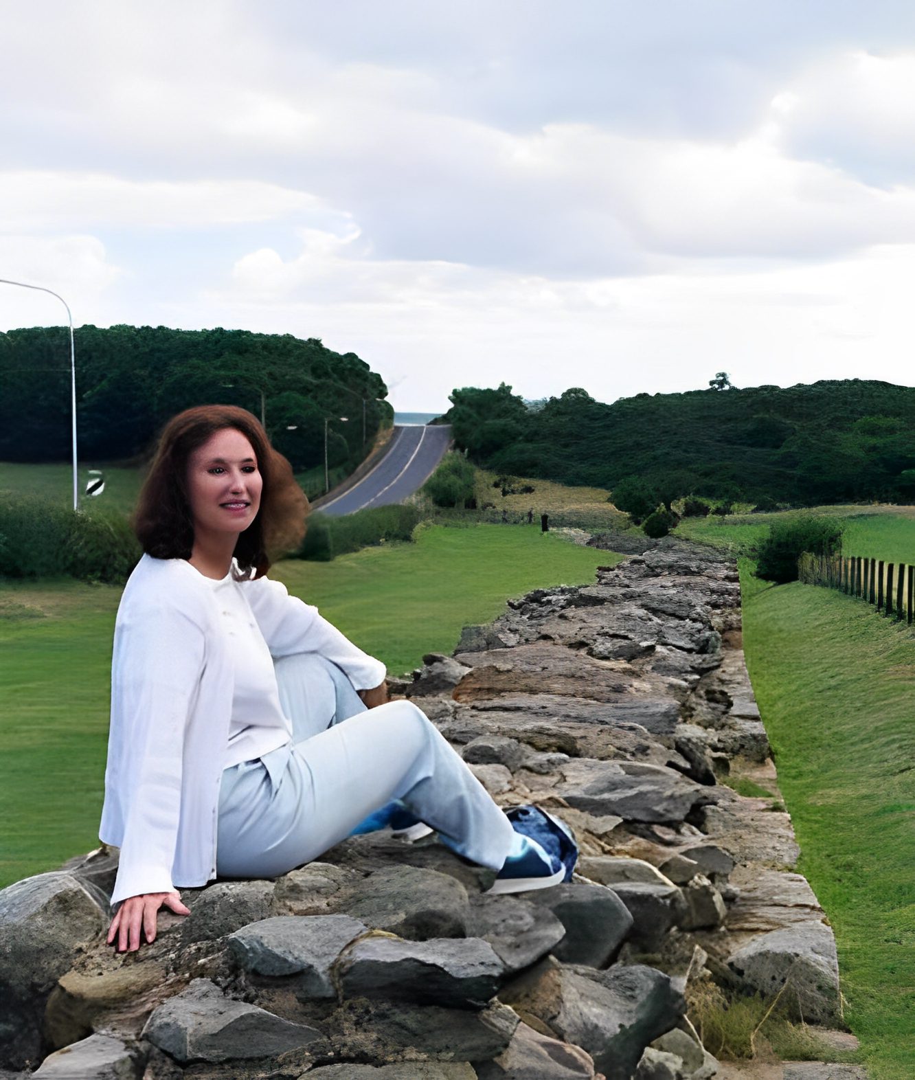 Woman sitting on rock wall beside road.